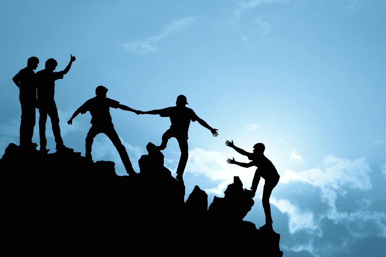 People helping each other climb a mountain
